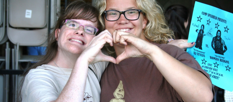 two female campers making a heart shape with their hands